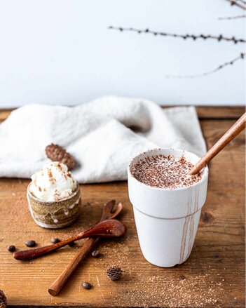 Auf dem Foto ist ein Becher mit heißer Schokolade zu sehen. Daneben ist auch ein Handtuch, Ein Zapfen und Löffel zu sehen. | © SONNENTOR